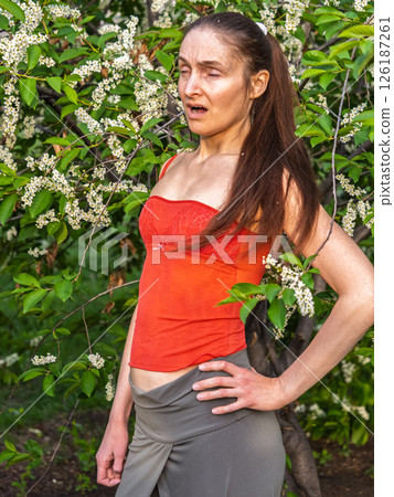 Young woman sneezes in the park against the background of a flowering tree. Allergy to pollen concept. Young woman sneezes in the park against the background of a flowering tree. Allergy to pollen concept. 126187261