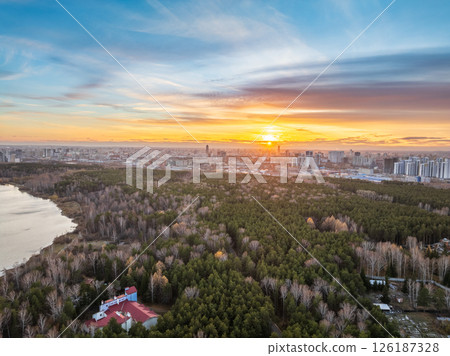 Autumn forest on lake shore at sunset and city on horizon, aerial view 126187328
