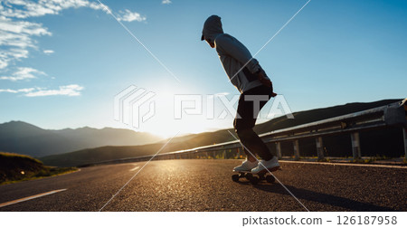 Skateboarder skateboarding on the sunset mountain top road Skateboarder skateboarding on the sunset mountain top road 126187958