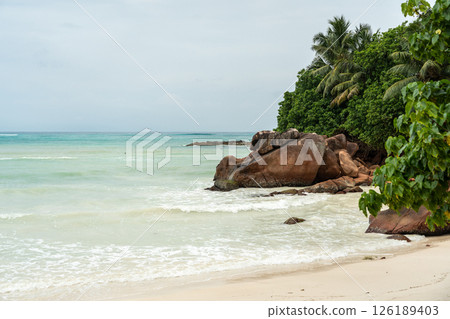 Tropical coast of Seychelles before rain, with cloudy sky, gentle waves, rocky islet Tropical coast of Seychelles before rain, with cloudy sky, gentle waves, rocky islet 126189403