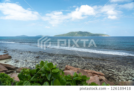 View of granite coastal rocks and ocean waves with distant islands on the horizon under cloudy 126189418