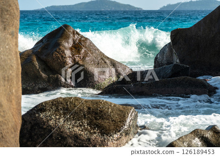Ocean and sea wave crash against rock and water along the beach shore under the blue sky 126189453
