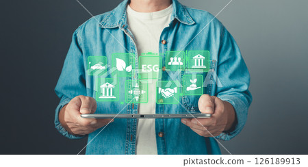 A person holds a tablet displaying ESG icons, representing sustainability, ecology, green energy, and responsible business practices for environmental, social, and governance initiatives. 126189913