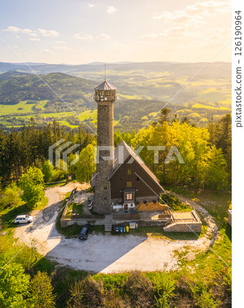 Drone captures an aerial view of Svatobor Lookout Tower surrounded by lush greenery and rolling hills in Czechia at sunset, showcasing the beauty of the landscape and architecture. Drone captures an aerial view of Svatobor Lookout Tower surrounded by lush greenery and rolling hills in Czechia at sunset, showcasing the beauty of the landscape and architecture. 126190964