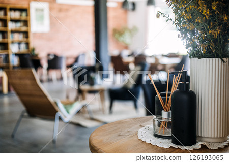 Close-up of aromatherapy diffuser, soap bottle, and potted flowers on a wooden table in a cozy lounge. Sensory wellness, interior mindfulness, cozy hospitality, slow cafe culture... 126193065