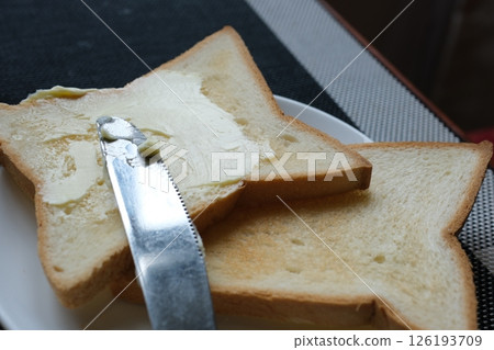 Spreading butter onto toast with knife on wooden board 126193709