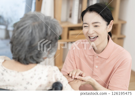 一位女性護理人員正在與一位坐在輪椅上的老年婦女交談 一位女性護理人員正在與一位坐在輪椅上的老年婦女交談 126195475