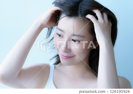 A young woman massaging her scalp with both hands. Photo courtesy of Tokyo Electronics College, Denpa Gakuen Corporation. 126195926