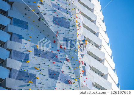 Climbers scale the tallest climbing wall in the world, located at Amager Bakke in Copenhagen, Denmark. The structure features colorful holds and stunning architecture against a clear blue sky. Climbers scale the tallest climbing wall in the world, located at Amager Bakke in Copenhagen, Denmark. The structure features colorful holds and stunning architecture against a clear blue sky. 126197696