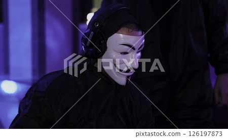 A masked figure stands in a dark space, vibrant lighting creates a dramatic, artistic atmosphere. Media 126197873