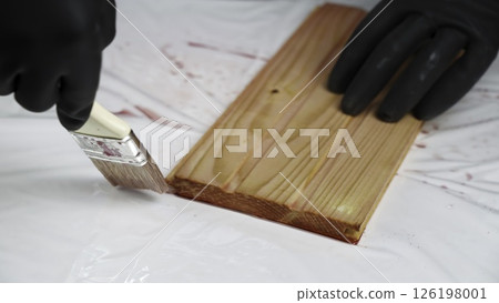 The process of Applying Wood Stain with a Brush on a Beautiful Wooden Plank Surface. Creative 126198001