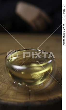 A delicate glass bowl with shimmering golden tea rests elegantly on a wooden surface. Media 126198125