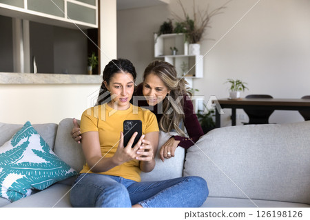 Happy adolescent daughter showing mature mom photo on phone screen 126198126