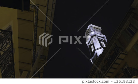 Majestic illuminated bell tower rising above buildings at night. Action Majestic illuminated bell tower rising above buildings at night. Action 126198128