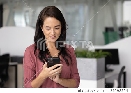 Young businesswoman in casual wear texting on phone in office 126198254
