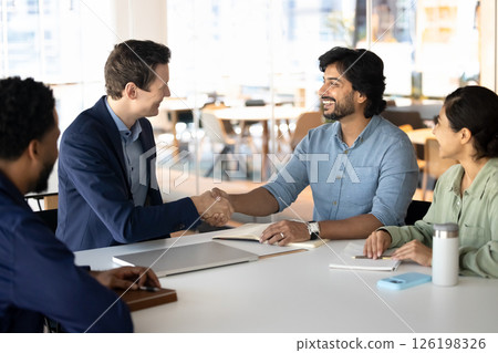 Two multiethnic business partners shaking hands seated at table 126198326