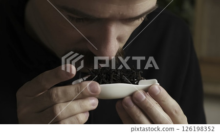 A person is savoring and appreciating the rich aroma of loose tea leaves placed in a bowl. Media 126198352