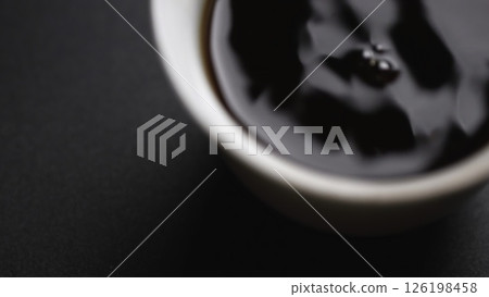 Gently pouring a rich liquid into a beautifully crafted white cup resting on a dark surface. Media 126198458