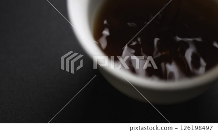 Gently pouring a rich liquid into a beautifully crafted white cup resting on a dark surface. Media Gently pouring a rich liquid into a beautifully crafted white cup resting on a dark surface. Media 126198497