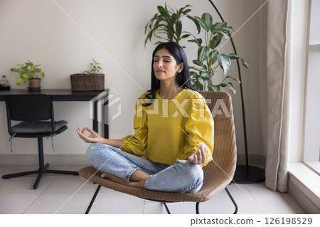 Peaceful young lady meditate sitting on armchair in lotus position 126198529
