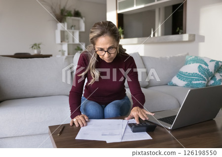 Concentrated senior woman working from home office checking financial report Concentrated senior woman working from home office checking financial report 126198550