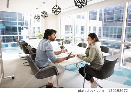 Two Indian colleagues engaged in focused discussion in modern office 126198672
