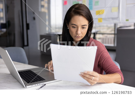 Serious young businesswoman review paper documents before typing on notebook Serious young businesswoman review paper documents before typing on notebook 126198783