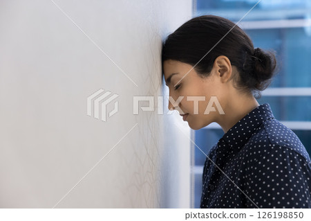 Woman employee lean her head against wall in workplace Woman employee lean her head against wall in workplace 126198850