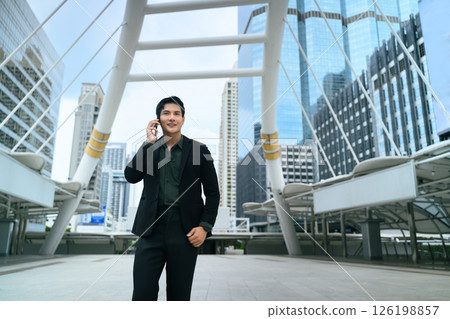 Successful businessman walking through a modern cityscape while talking on his phone Successful businessman walking through a modern cityscape while talking on his phone 126198857