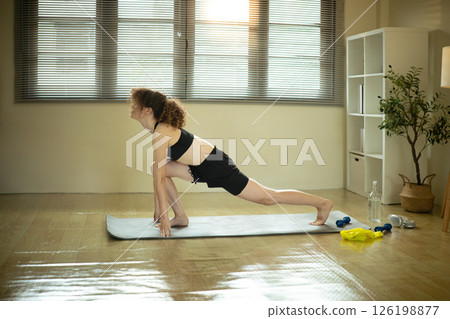 Young woman stretching on yoga mat in a cozy home, practicing fitness and flexibility 126198877