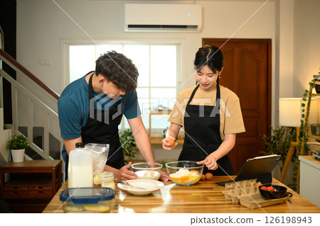Young couple cracking egg into flour while preparing pancake batter together 126198943