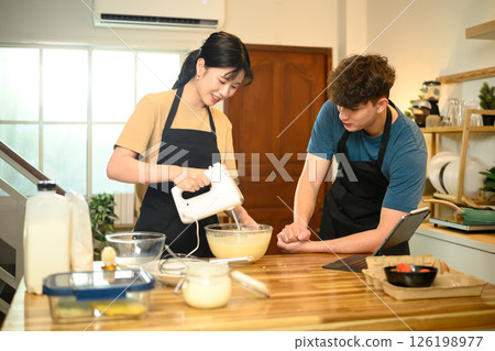 Smiling couple making pancake batter together using a hand mixer in a kitchen 126198977