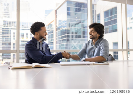 African and Indian business partners shaking hands seated at table African and Indian business partners shaking hands seated at table 126198986