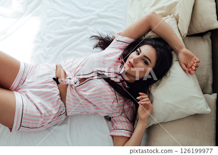 brunette woman in pajamas in white bedroom on bed sleep brunette woman in pajamas in white bedroom on bed sleep 126199977