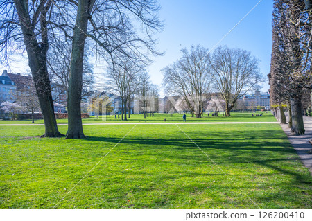 Visitors enjoy a peaceful afternoon at Rosenborg Castle Gardens in Copenhagen. The lush green lawn is bathed in sunlight, inviting relaxation and leisurely strolls among the trees. Visitors enjoy a peaceful afternoon at Rosenborg Castle Gardens in Copenhagen. The lush green lawn is bathed in sunlight, inviting relaxation and leisurely strolls among the trees. 126200410