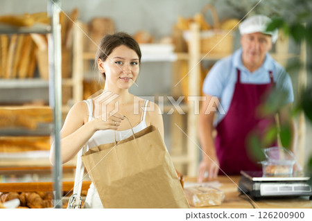 Portrait of young girl buyer with paper bag of fresh baked goods in interior of bakery Portrait of young girl buyer with paper bag of fresh baked goods in interior of bakery 126200900