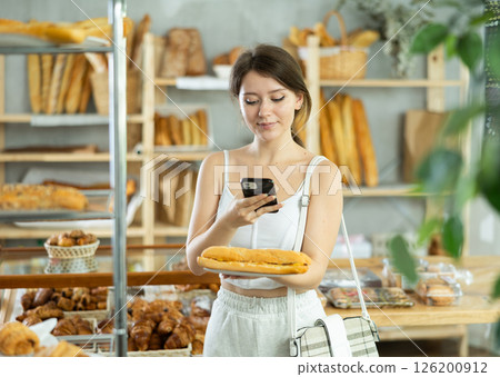 Female customer scanning QR code on label of fresh baked goods in bakery interior 126200912