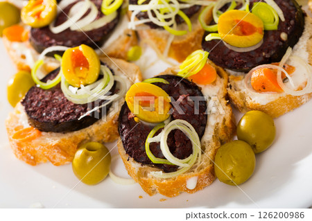 Tasty canapes with blood sausage, bread, olives and onion at plate Tasty canapes with blood sausage, bread, olives and onion at plate 126200986