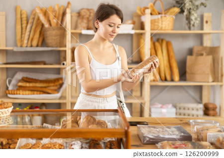 Young female customer stands with cookies in hands near window of bakery. 126200999