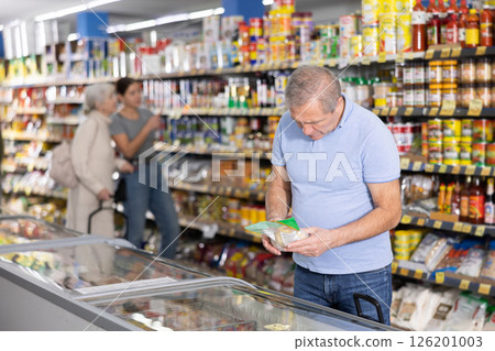 Senior man looking at products in glass refrigerator in food store 126201003