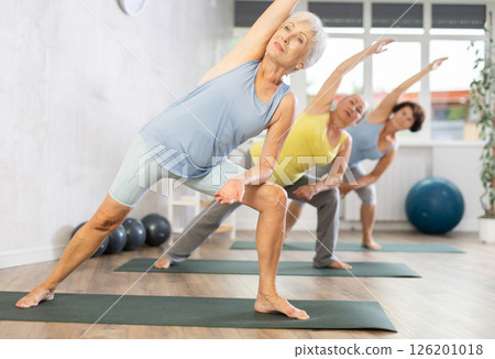 Old woman practicing extended side angle pose of yoga in training room during fitness classes 126201018
