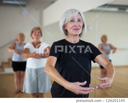 Portrait of a mature woman and people standing in the 1st position of the ballet stand in a dance studio 126201145