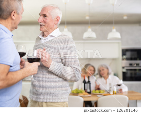 Elderly men have withdrawn from their female companions, stand with glass of wine in hands, chatting 126201146