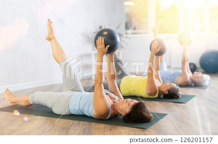 Elderly women perform softball exercises lying on floor, workout for beautiful figure, toned body 126201157