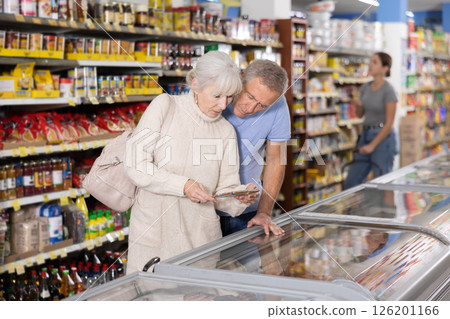 Senior couple looking at goods in glass showcase in supermarket 126201166