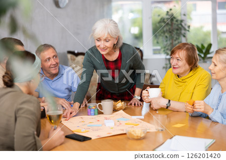 Smiling elderly woman with friends playing board game Smiling elderly woman with friends playing board game 126201420