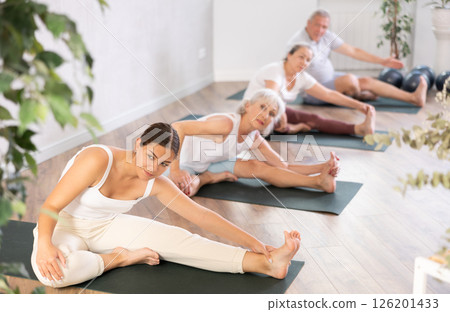 Mature positive women doing body stretching in yoga class Mature positive women doing body stretching in yoga class 126201433