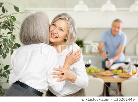Two elderly women friends hugging in kitchen 126201449