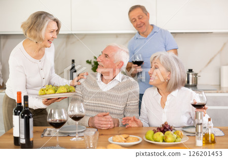 During feast, elderly housewife sets table, puts on desk snack for wine, large platter with fruits During feast, elderly housewife sets table, puts on desk snack for wine, large platter with fruits 126201453