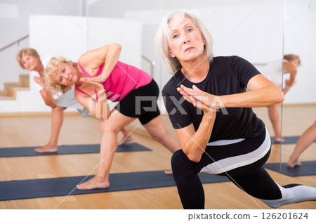 Aged woman practicing Parvritta Parsvakonasana during group yoga training Aged woman practicing Parvritta Parsvakonasana during group yoga training 126201624
